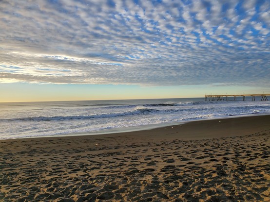 A grand opening, with many swirly puffy clouds in a bright blue sky, with darker blue water down below.