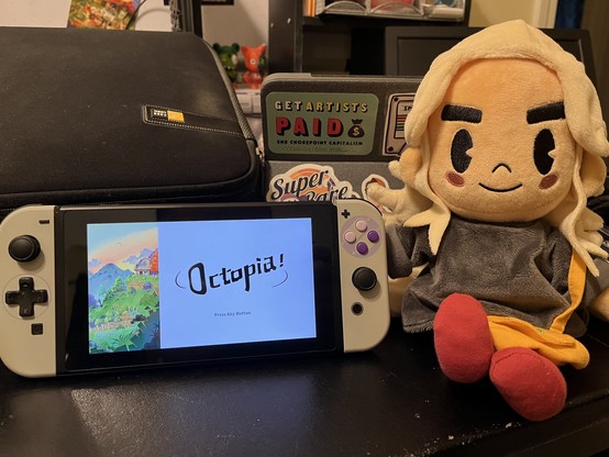 An Nintendo Switch sitting on a desk on the title screen for Octopia—right side of the screen just has the title with “press any button” underneath, while the left shows a house on the top of an uneven hill at dawn. Said hill is flourishing with greenery with some fencing and empty plots of land for crops. To the left of the Switch is Sam from Eastward with white hair, wearing a grey shirt and red shoes. She is also carrying a golden-yellow tote bag.