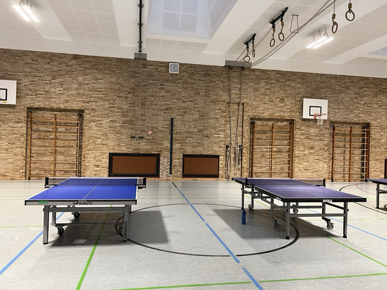 Zwei Tischtennis-Platten in einer Turnhalle, an denen gerade nicht gespielt wird 