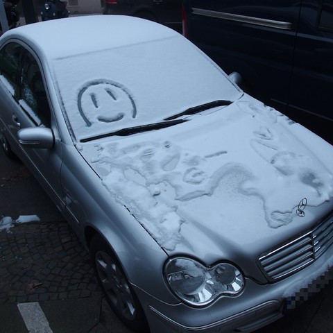 Im öffentlichen Raum abgestelltes Auto mit ca 2 cm Schnee auf Dach, Frontscheibe und Kühler; der Schnee ist ca 2 oder 3 Tage vorher gefallen und im Straßenraum größtenteils schon wieder getaut.
Jemand hat einen smiley in den Schnee auf der Frontscheibe gezeichnet.