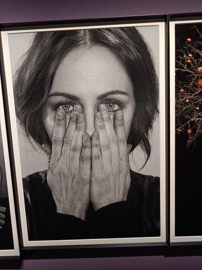 A woman has hidden her face with her hands. Her eyes look straight into your eyes 