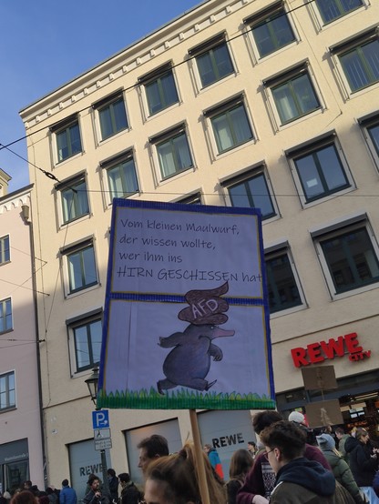 Schild mit dem Maulwurf aus dem Kinderbuch "Vom kleinen Maulwurf, der wissen wollte, wer ihm auf den Kopf gemacht hat" und AfD als *Kopfbedeckung*💩. Darüber der Titel:
Vom kleinen Maulwurf, der wissen wollte, wer ihm ins HIRN GESCHISSEN HAT