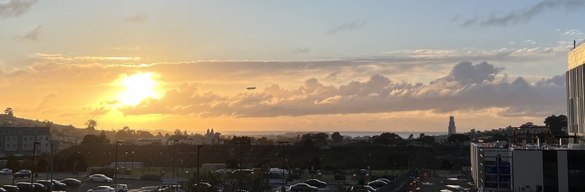 Sunset with vibrant sky over urban landscape, silhouette of buildings, and a blimp in the sky.