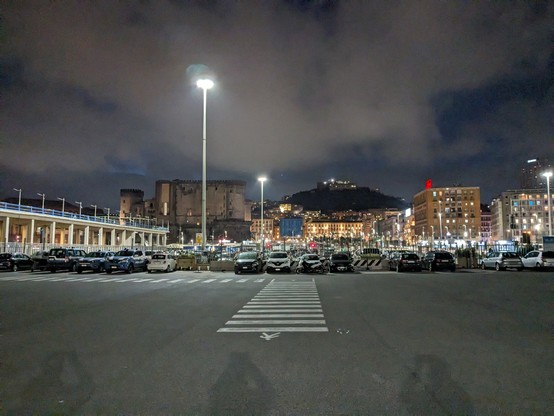 A brightly lit parking lot under a cloudy night sky. Castles and hills in the distance.