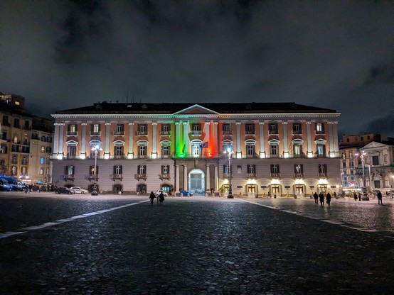 A stately palazzo at night, lit up in green, white, and red.