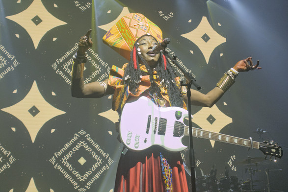 Fatoumata Diawara on stage at Koko. She has a white electric guitar slung around her neck and is holding her arms out wide as she sings.