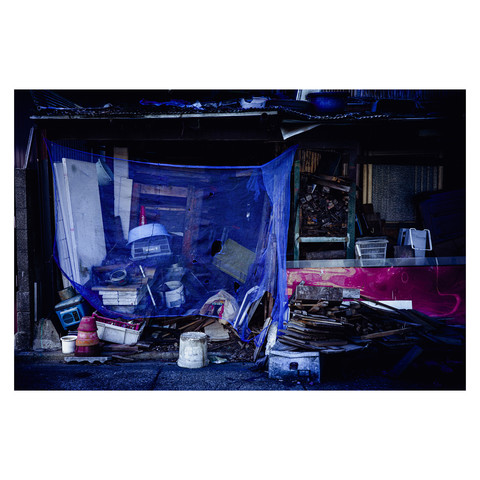 What's captured here is a moment where everyday refuse gains an almost mythical protection. A netting, not just a practical deterrent, becomes a barrier between worlds. The pile of wood, plastic, and the ghostly shadows invite stories of a nocturnal life where the ordinary becomes the shield against the extraordinary.