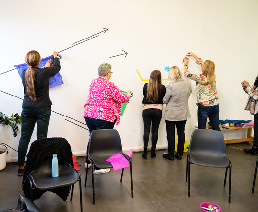 People stick coloured paper onto a white wall, in what looks like an art conference setting.