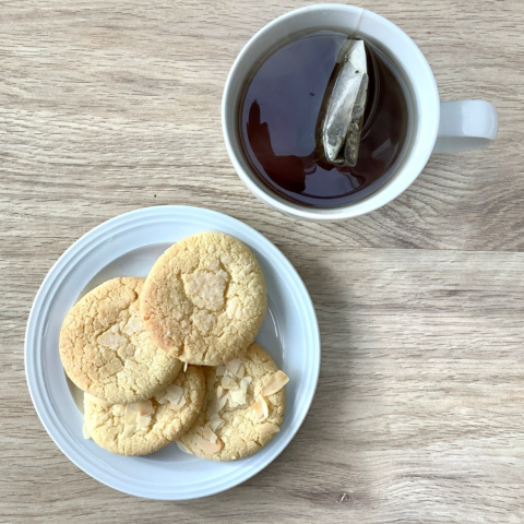 A white plate with 4 cookies on it, and a large mug with tea shown from above on a light wooden background.