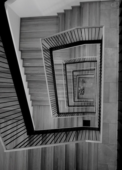 b/w photography
rectangular staircase from above
wooden stairs and black metalic handrail