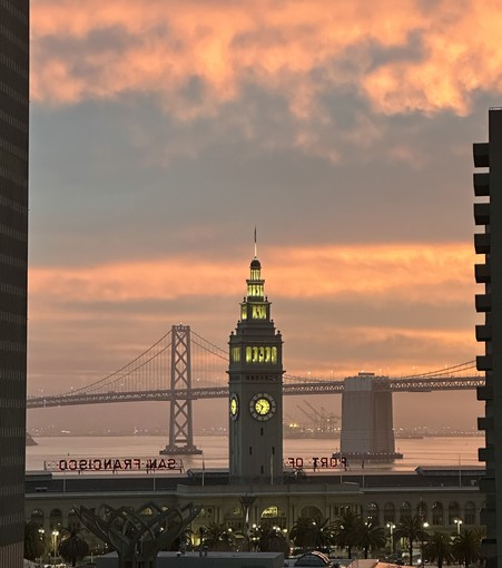 View of the San Francisco Bay Bridge and Ferry Building clock tower at sunrise.