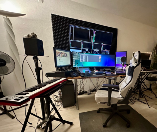 GPT:


Ein professioneller Homeoffice-Arbeitsplatz ausgestattet für 3D- und Videoproduktionen. Er verfügt über mehrere Monitore, die über einem großen Schreibtisch angeordnet sind, mit geöffneten Anwendungen und Programmierumgebungen. Ein Keyboard auf der linken Seite und ein Laptop auf einem separaten kleinen Tisch deuten auf musikalische Aspekte der Arbeit hin. Ein ergonomischer Stuhl steht im Zentrum, bereit für den Nutzer. Die Wand ist mit schalldämpfenden Platten ausgekleidet, was auf eine Nutzung für Audioaufnahmen hindeutet. Ein Ventilator und eine Zimmerpflanze fügen dem Raum eine persönliche Note hinzu, während das Mikrofon auf dem Ständer in der Mitte für Sprach- und Gesangsaufnahmen bereitsteht. Kabel verlaufen über den Boden und hinter dem Schreibtisch, was auf eine komplexe technische Ausstattung schließt