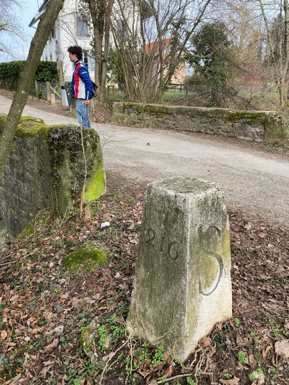 A border stone un the foreground, next to an old stone bridge. The Swiss old border guard’s house is visible in the background 