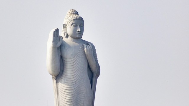 Gian white standing Buddha statue in front of an overcast sky.