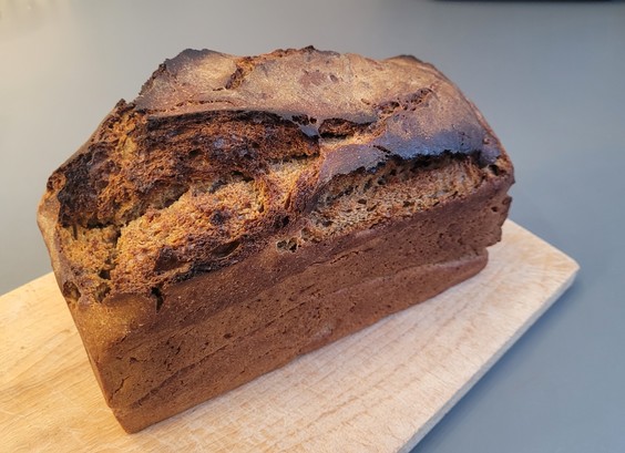 Farbfoto:Ein einfaches, gut hochgegangenes Kastenbrot mit entsprechend aufgerissener Kruste oben liegt auf einem Schneidebrett. 