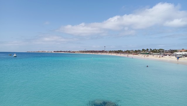Ein langer, zu weiter Bucht gebogener Sandstrand, relativ wenig Leute am Strand