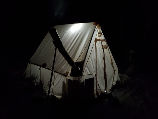 a canvas hot tent and wood stove glowing gently against the dark. the tent is set up in the woods of northern Ontario.