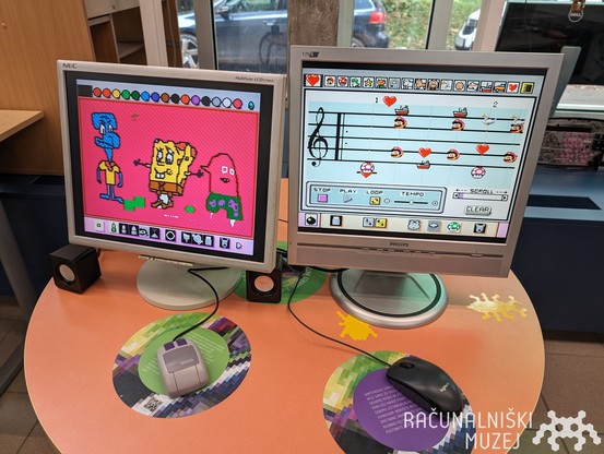 two computer screens with visible drawings, Nintendo SNES mouse, a Logitech mouse and small speakers