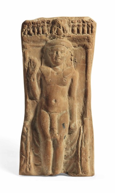 The young god Harpokrates is depicted in the nude with a large phallus, seated on a draped throne, wearing the nemes headdress surmounted by a hemhem-crown, with his left arm held by his side, his right arm raised up in blessing, a frieze of uraei above, a circular vent hole at the back.