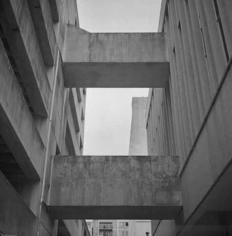 A black and white film photo. Two concrete skyways hover over an alley in downtown Austin, Texas. Thursday, January 25, 2024.