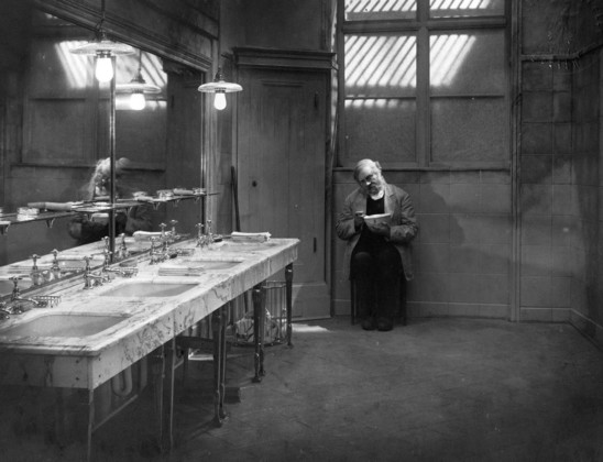 B&W still from The Last Laugh (1924), row of sinks in a wash room empty except for a forlorn looking attendant eating a bowl of soup.