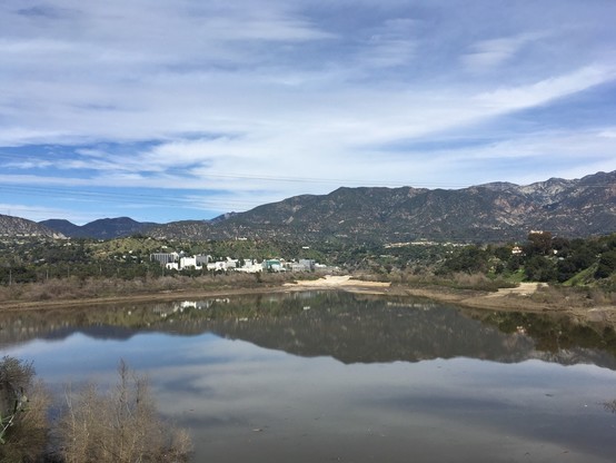 The JPL campus sits at the far end of a still lake, with mountains in the background. It’s a sunny day with thin, high clouds
