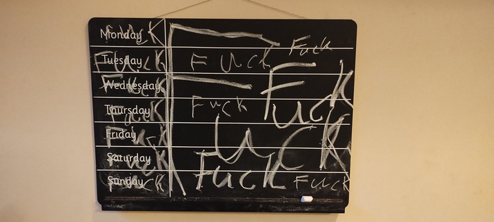 A week planner blackboard with the word "fuck" scrawled over it everywhere possible.
