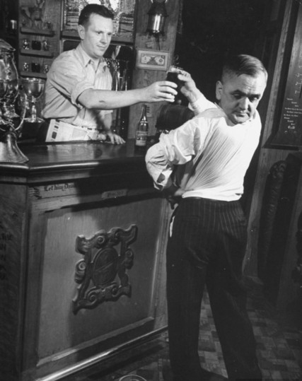 Hombre, qué ha girado la cabeza hasta tener la cara orientada hacia la espalda, pidiendo una cerveza en la barra de un bar.