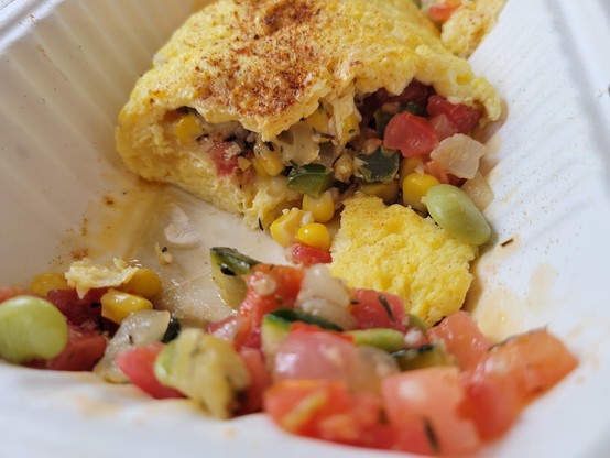 Succotash omelet, partially eaten, in a white paperboard to-go container