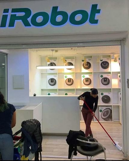 A female human cleaner cleans the floor of a store that sells robotic vacuum cleaners.