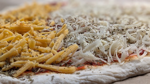 Pizza vor dem Backen mit Käse bestreut.