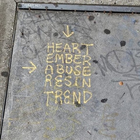 A section of sidewalk where a tagger has written a word square. This can be read horizontally or vertically and it says: Heart, ember, abuse, resin, trend.