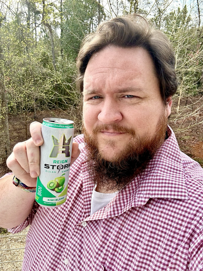 Me, a man with short hair and a beard. I'm wearing a button-up shirt with a checkered pattern, and holding a can of Reign Storm Kiwi Blend energy drink.