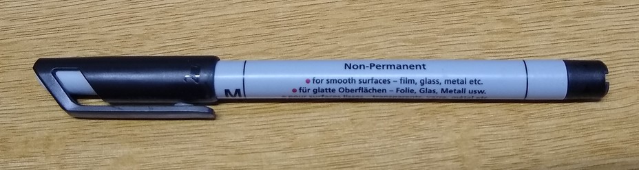 Picture of a pen, lying on a desk surface.
On the pen it says "Non-Permanent / for smooth surfaces - film, glass, metal etc.

Not shown:
In another place it describes the pen as a "OHPen" (i.e. overhead projector pen)