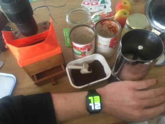 Smartwatch zeigt 13:12 an.
12 bis 13 Volt Kaffeemühle, Lifehack mit Akkuschrauber umgebaut, leere Tomatendosen, Espressokanne, Äpfel, Lützerath-Sticker in 80er-Jahre Küche.