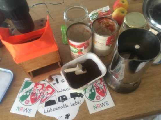 12 Volt Kaffeemühle, improvisiert mit Akkuschrauber umgebaut, leere Tomatendosen, Espressokanne, Äpfel, Lützerath-Sticker in 80er-Jahre Küche.
