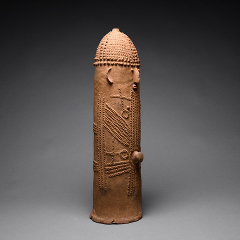 It's a terracotta phallus with a human face, including ears protruding from its sides. Its head and body are greatly adorned with small incisions and reshaped clay, creating beautiful details. The Bura culture refers to a set of archeological sites in the lower Niger River valley of Niger and Burkina Faso.