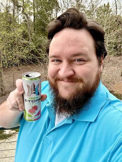 Me, a man with short hair and a beard. I'm wearing a polo shirt and holding a can of Reign Storm Guava Strawberry energy drink.