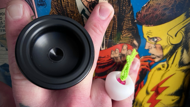 In hand, a black pom Mojo set up for 5A freehand play with a white counterweight. The cover of Flash comics 189 behind. 
