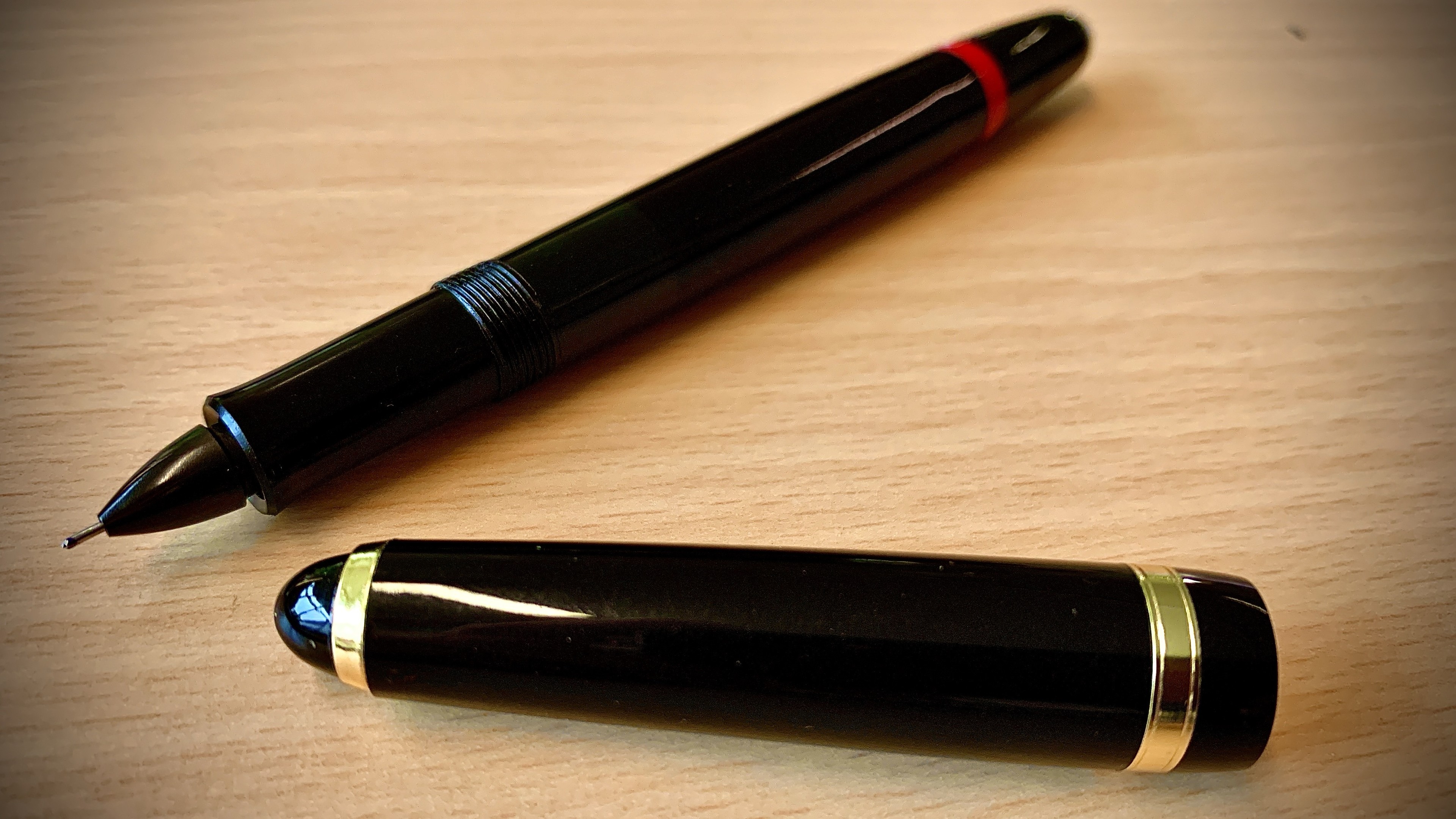Black fountain pen with its cap placed beside it on a wooden surface.