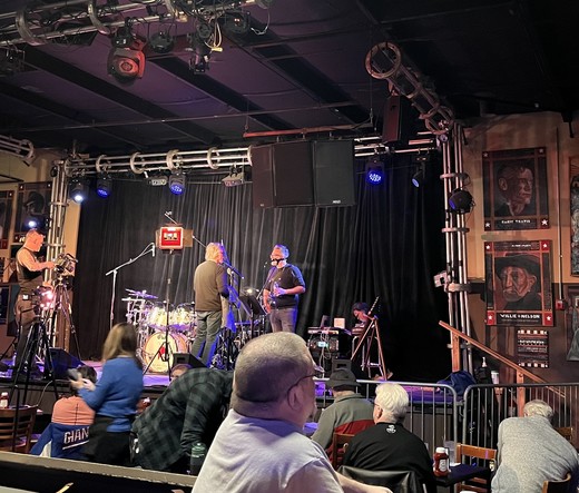 A terrible phone-photo of 3 men on a small club stage. At left is a roadie. At center with his back to us is the incomparably uncategorizable drummer Pat Mastelotto, and at right is the touch guitar wizard Markus Reuter. Soon, these very normal men will become 2/3 of Stick Men and start making beautifully pretentious music.