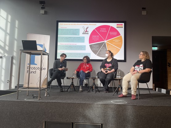 Panel: Tobias (Moderator) sitzt auf der Bühne mit Nadine vom Projekt Polychat, Karo von Rosenpass und Marta von QubesOS