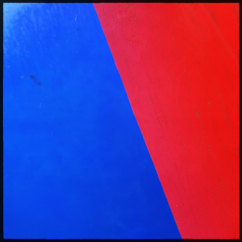 Abstract blocks of colour formed by the juxtaposition of the local recycling bins. Each metal bin is painted in a primary colour. Generally unattractive, this perspective brings a splash of colour from otherwise boring urban furniture. Here: blue against red.