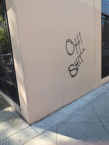 Simple graffiti tag on the side of a wall: OH! SHIT