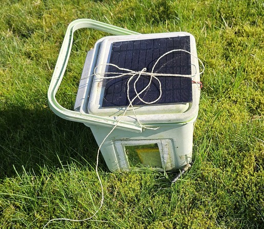 Kleiner Eimer mit Solarpanel drauf. Darin befindet sich ein Lorawan-Knoten und ein Mikrofon. 