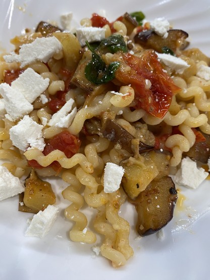Chunks of white sheep’s milk ricotta salata, half-spheres of red cherry tomatoes, wedges of thin purple and green eggplant atop long curly strands of yellow pasta in a flat, white bowl