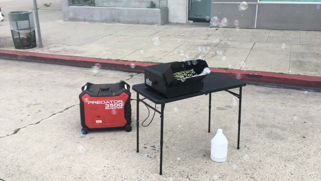 Brief video of a bubble machine blowing large numbers of bubbles as it sits on a small folding table, powered by a portable generator with the large-printed brand name PREDATOR