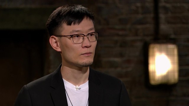 A photo of Dr. Chang Liu, wearing a white t-shirt, a black jacket, and glasses, demonstrating Extend Robotics' technology on the BBC television show Dragons' Den.
