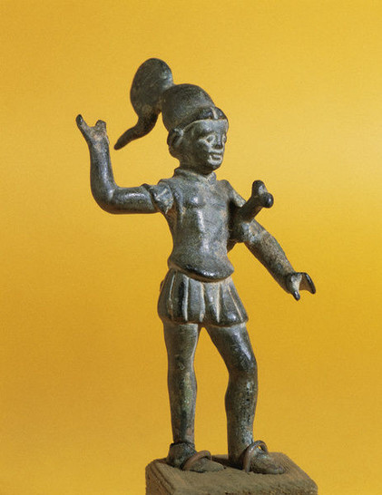 Bronze statuette of Mars, the Roman God of War, wearing a crested helmet, a muscle cuirass, and his sword girded around his shoulder. He probably used to hold a spear in his raised right hand, now lost.