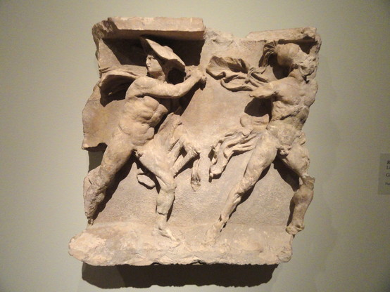 This carved limestone relief depicts two warriors striding to the right, one wearing a broad traveler's hat called a petasos and the other a Corinthian helmet. Each wears a short cloak called a chlamys over his left arm (now missing on the righthand warrior). The left warrior looks back, perhaps toward a horseman, since a small fragment of a horse’s foreleg remains behind his knee. The strong diagonals of the warriors contrasted with the flowing drapery of their cloaks demonstrates a dynamism c…